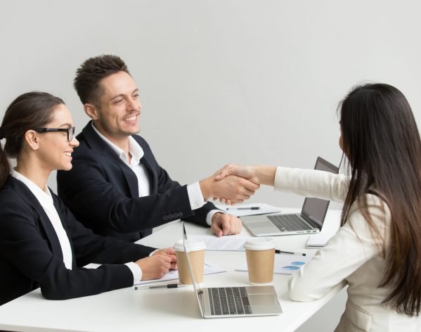 Friendly satisfied partners handshaking at group meeting thanking for successful teamwork, smiling millennial businessman shaking hand greeting businesswoman, respect or making contract deal concept